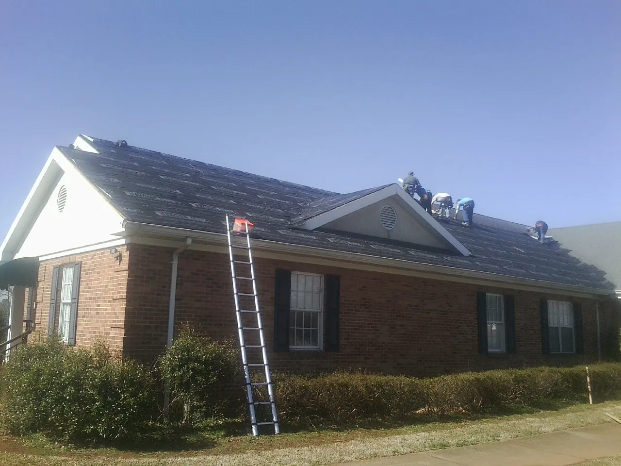 Crew tearing shingles off a brick ranch roof with a ladder set — Metal Roof Repair work by our crew in Fort Valley