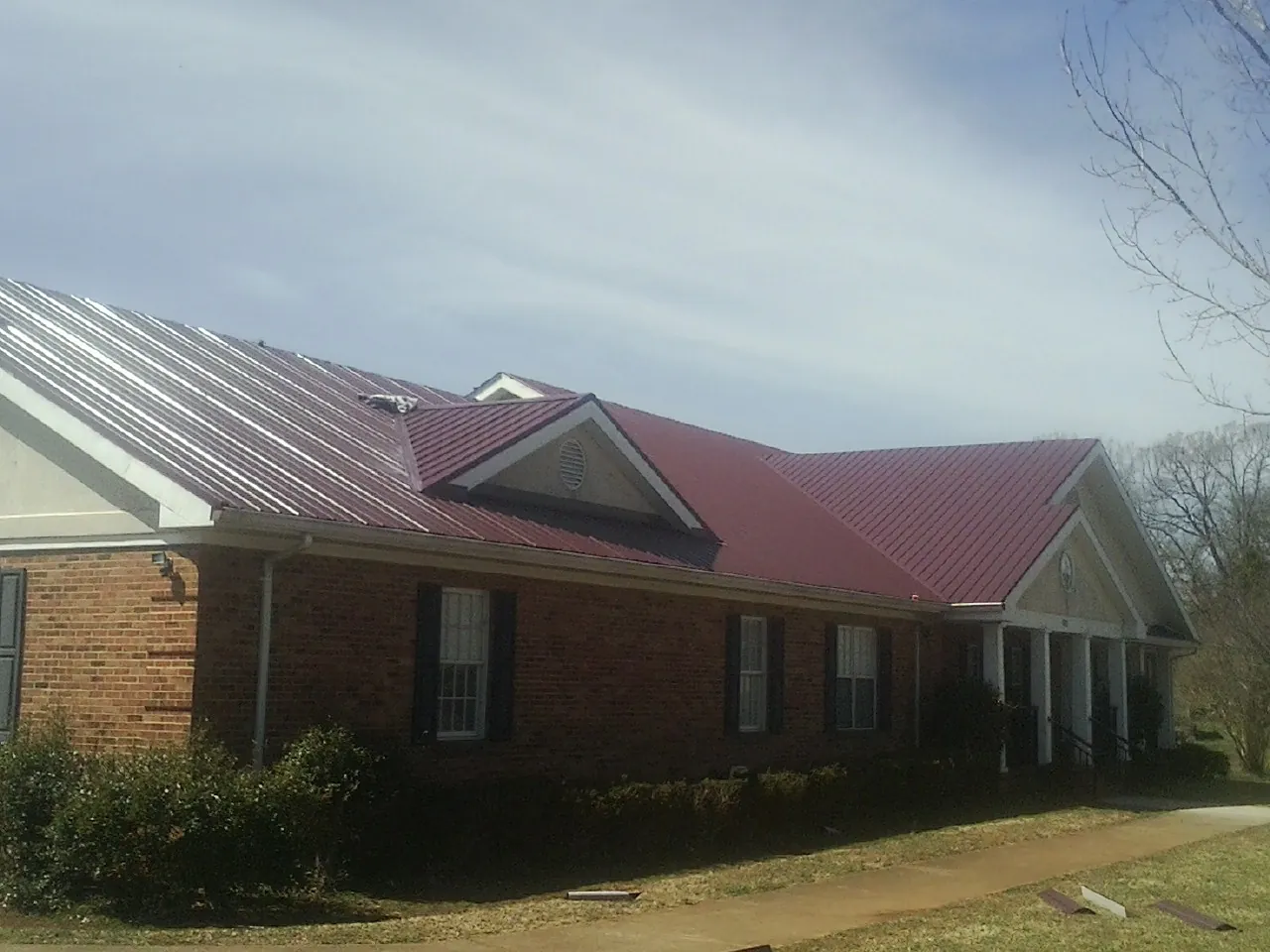 Red metal roof with gabled entries on a long brick building, from a Hail Damage Roof Repair job in Fort Valley