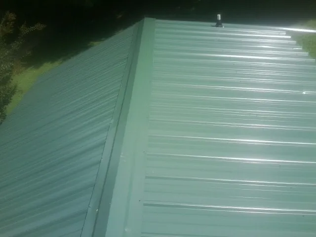 New green metal panels meeting at the ridge of a roof — Flat Roof Repair work by our crew in Fort Valley
