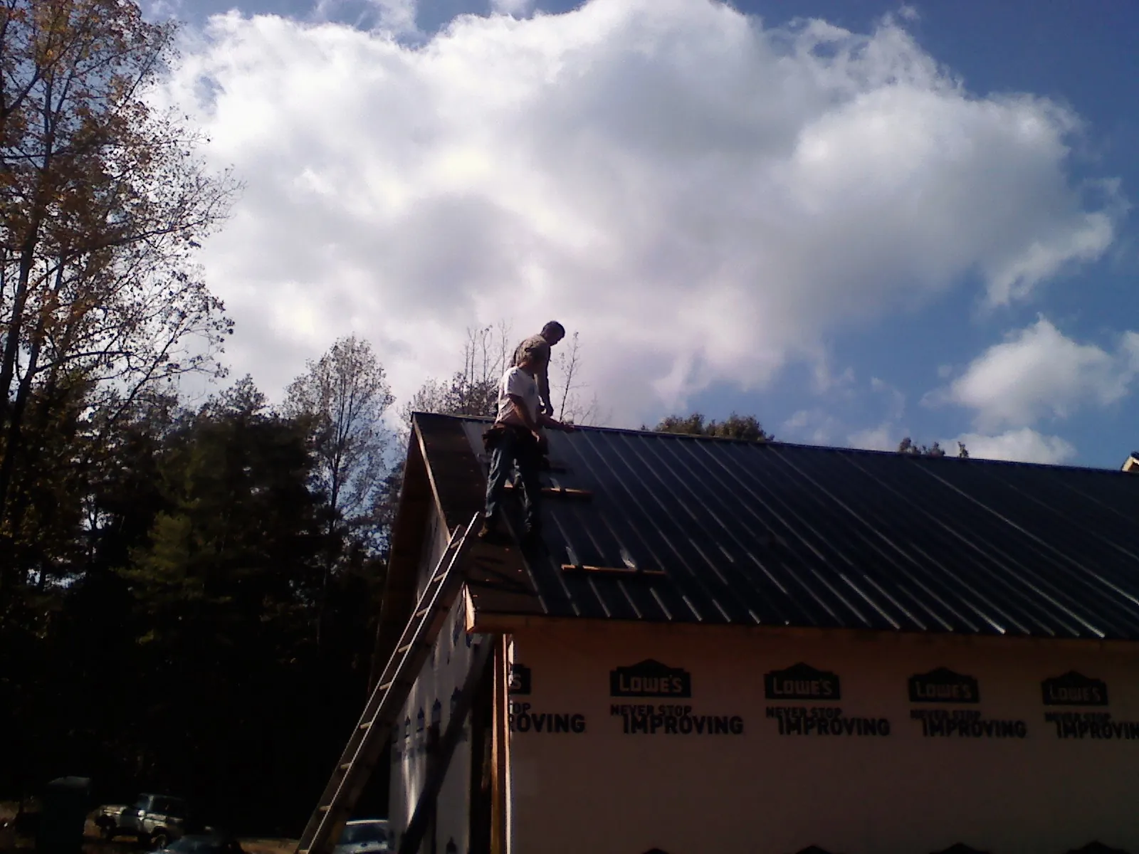 Roofer fastening dark metal panels high against a cloudy sky, from a Roof Inspection job in Fort Valley