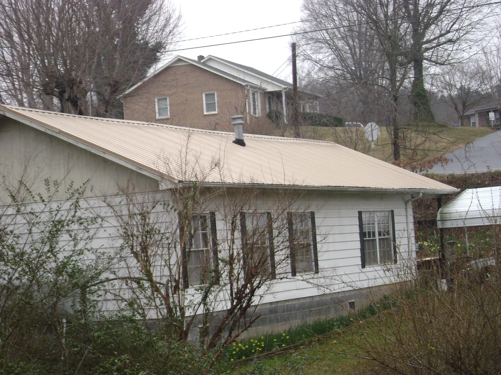 Tan metal roof on a white sided house set into a hillside — Commercial Roofing by Roofing Brothers in Fort Valley