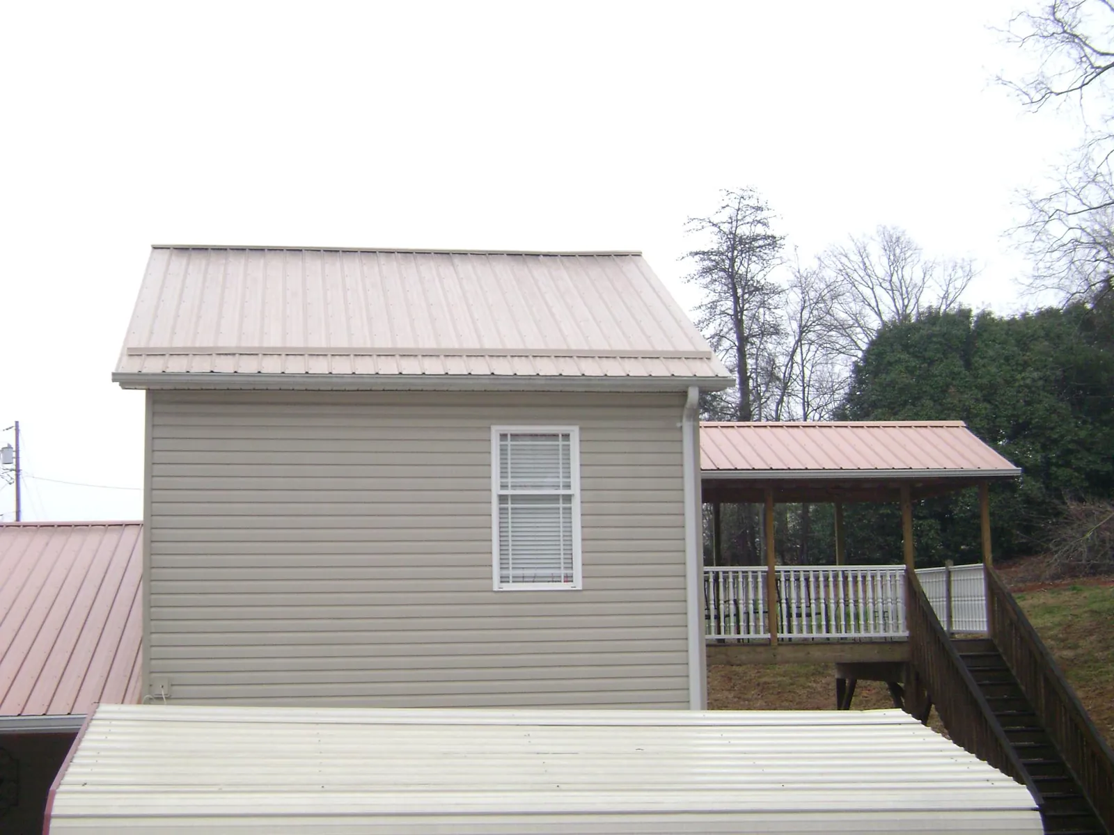 Tan metal roofs on a two story addition and attached porch, from a Roof Replacement job in Fort Valley
